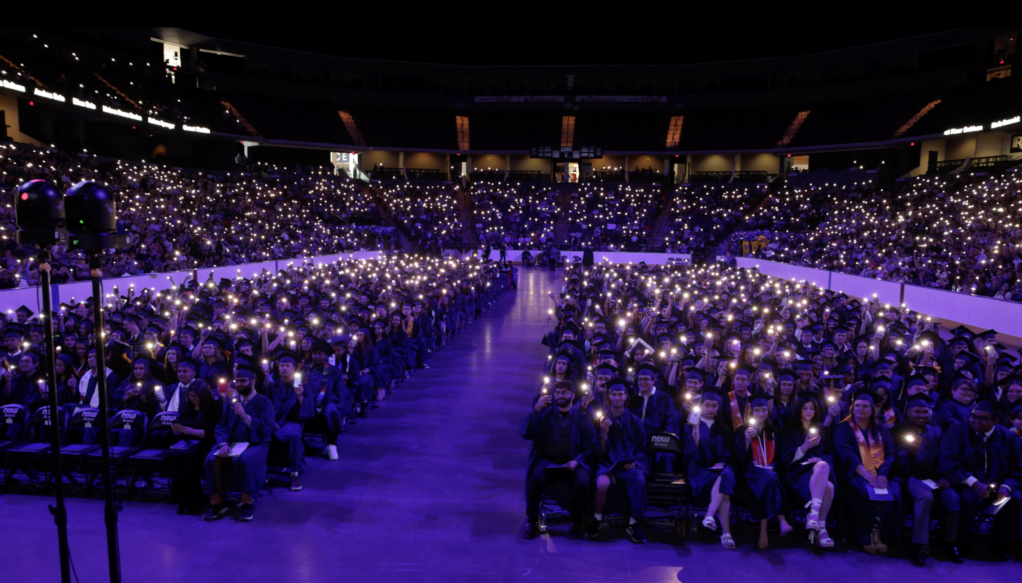 Graduates hold cell phone lights in darkened arena