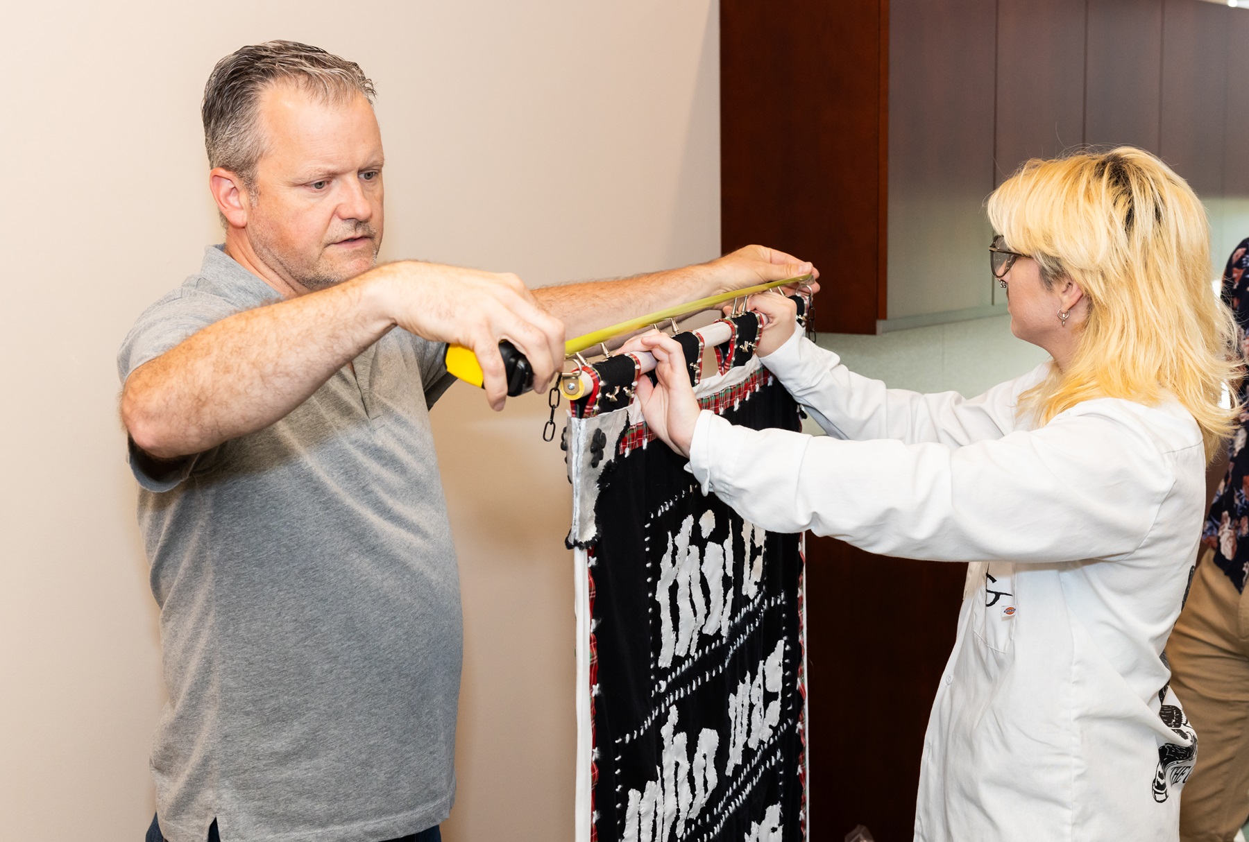 Professor Jason Peot and Lain Dennis hang Lain's artwork in the President's Office.