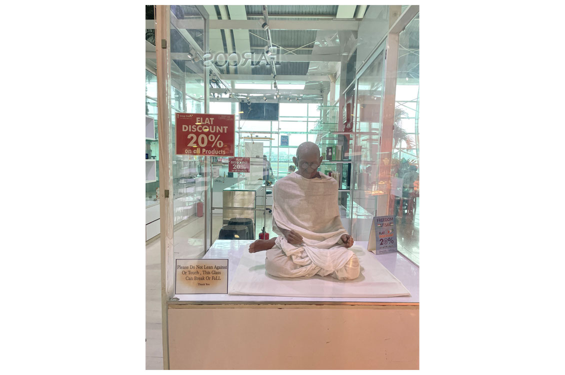 photograph of a sculpture of ghandi advertising a sale at a nearby shop