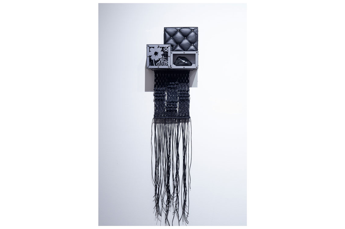 abstract wall sculpture of panels with fabric textures and macramé fringe at the bottom