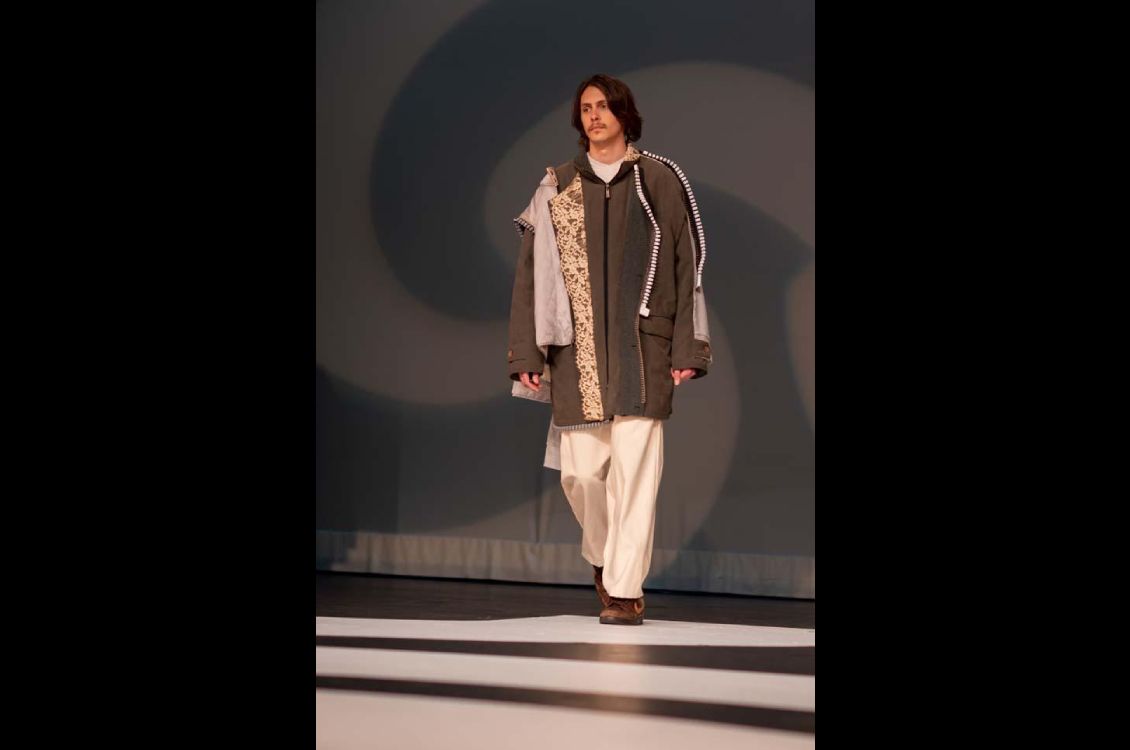 Man walking on stage with a layered multipatterned jacket and white pants