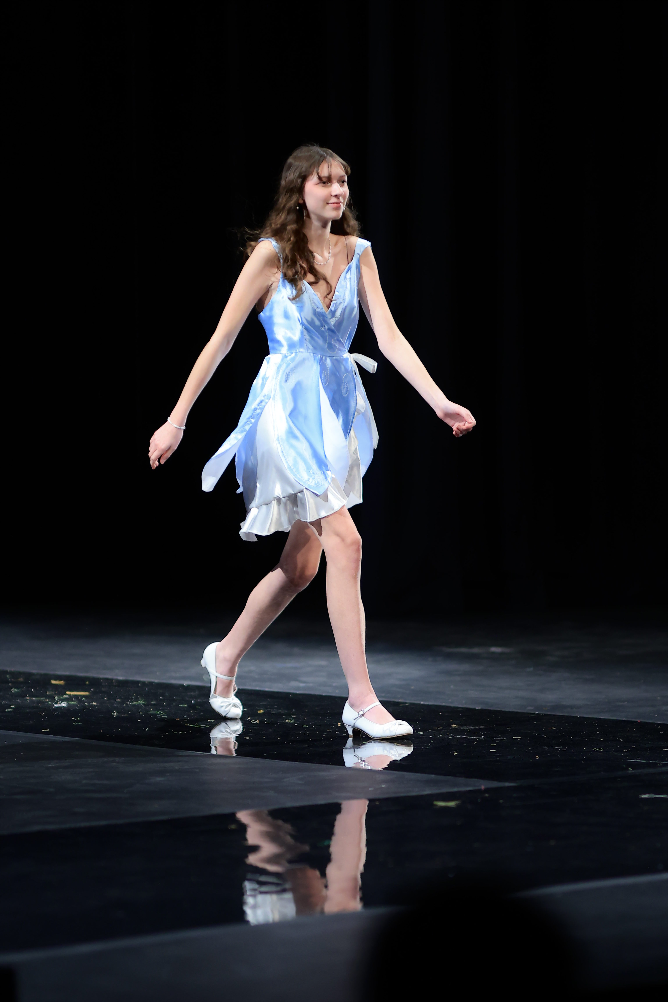 A model gracefully walks the runway in a chic sleeveless light blue and white dress, perfectly paired with matching light blue shoes.