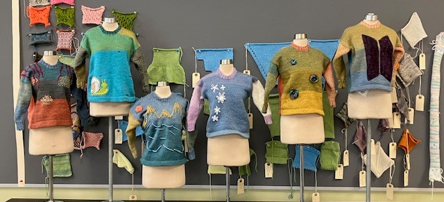 Colorful hand-knitted sweaters and swatches on display in a textile studio.