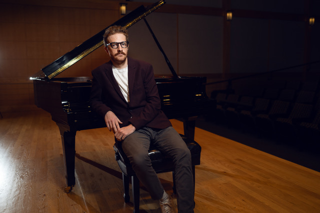 Ryan Wolfe seated at a piano, facing the viewer on a stage