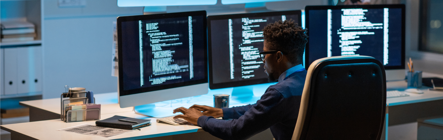 Man working at a desk with multiple monitors displaying code.