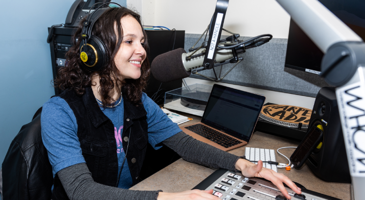 A student wearing headphones sits at a small mixing console and a microphone for the Harper College radio station.