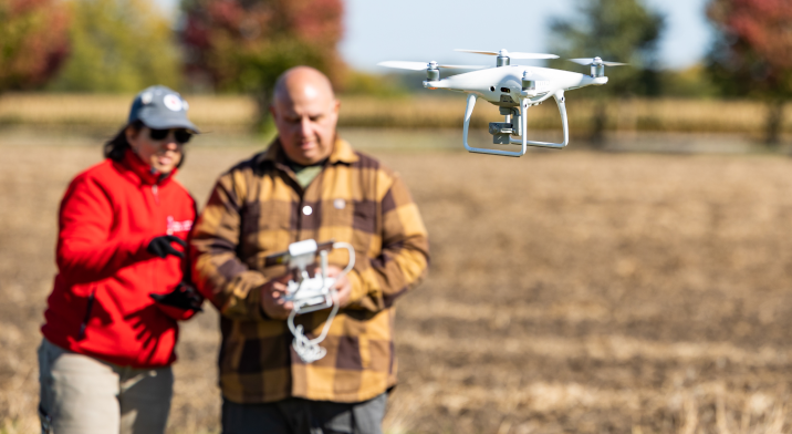 Two people flying a drone that hovers in front of them.