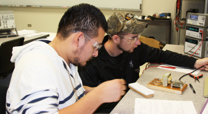 Two students sit at a table and work on a project with electrical wires.