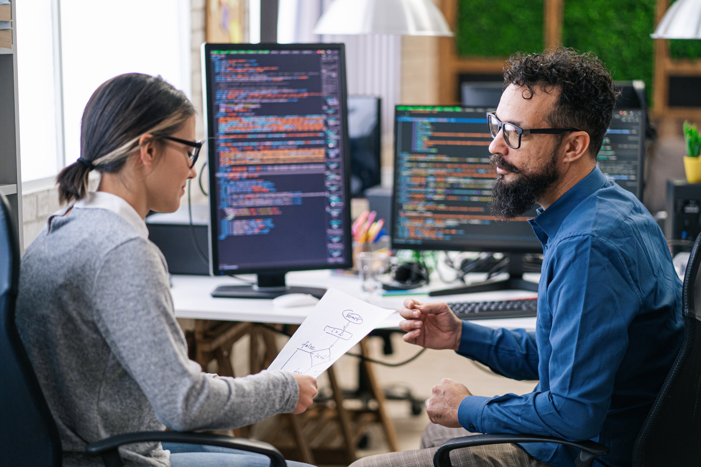Cloud computing professionals sit at a desk with lines of code on their displays.