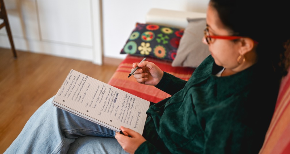 a woman sitting on her couch and writing a to-do list in a journal, viewed from above