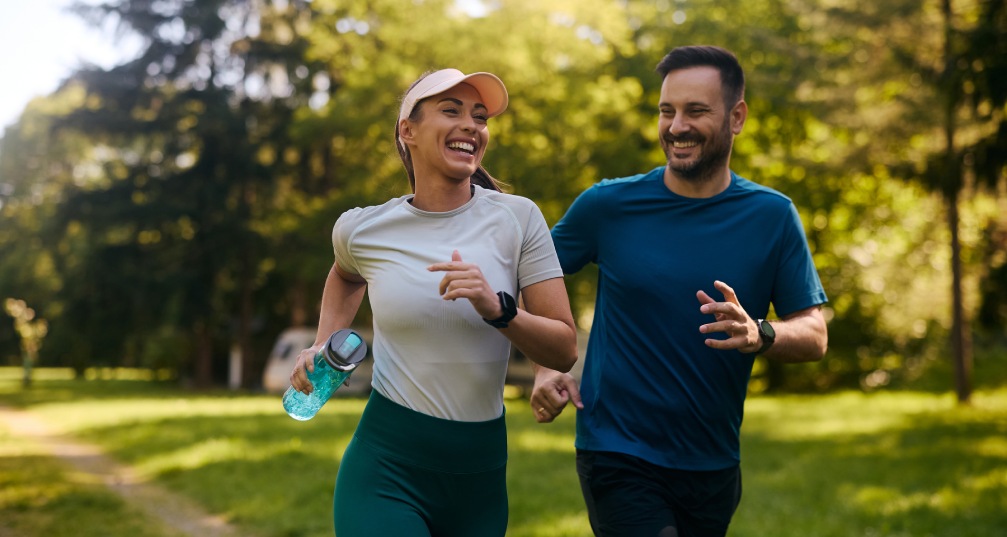 a man and woman jogging through a sunny park