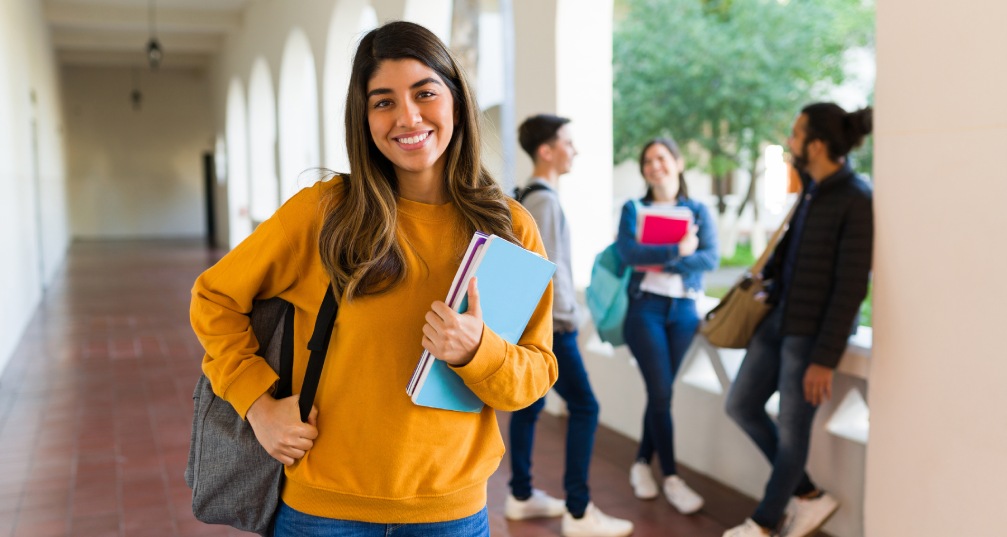 a young woman stands proudly with her backpack and school supplies