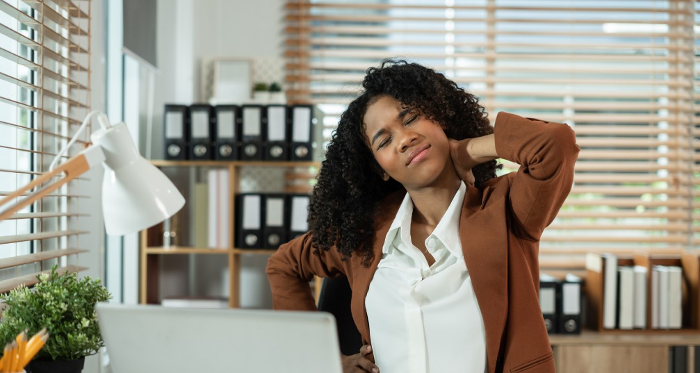 a woman stretches her neck as she sits at her desk