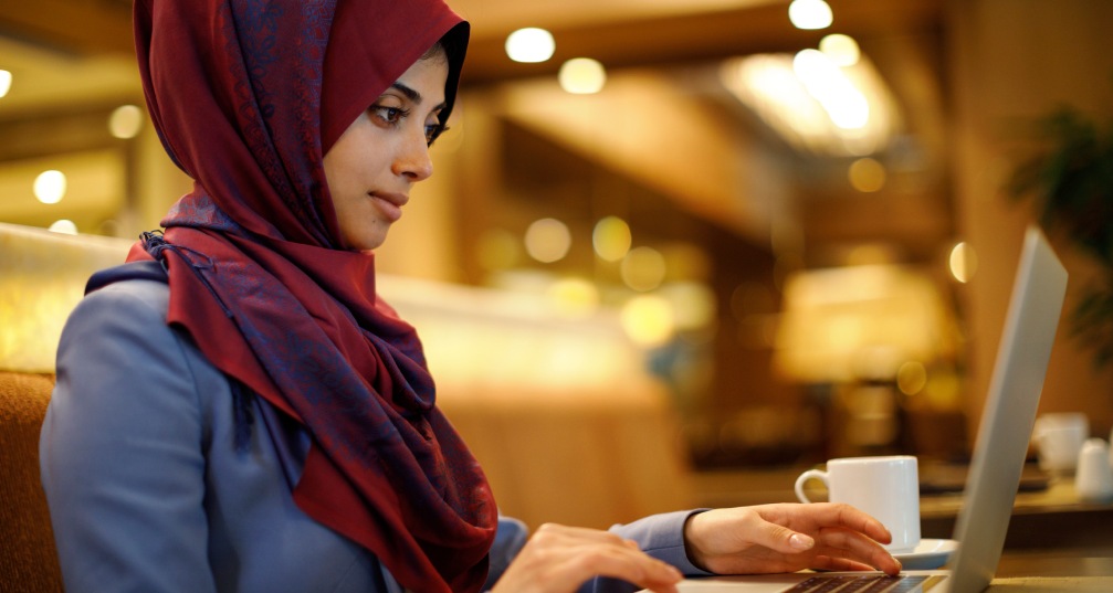 a woman sitting in a cafe with a cup of coffe and typing on her laptop