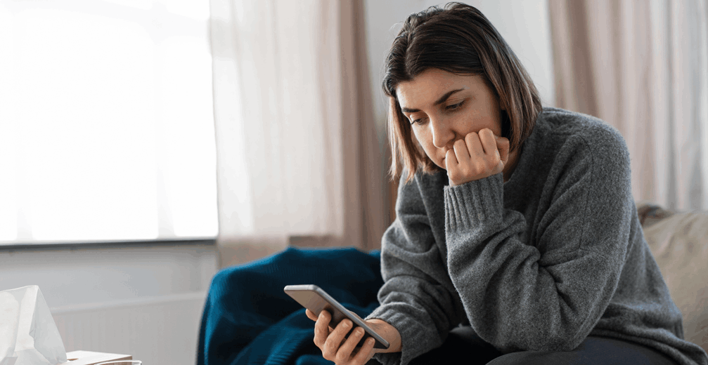 Woman looking at a phone and reading news in a bright room.