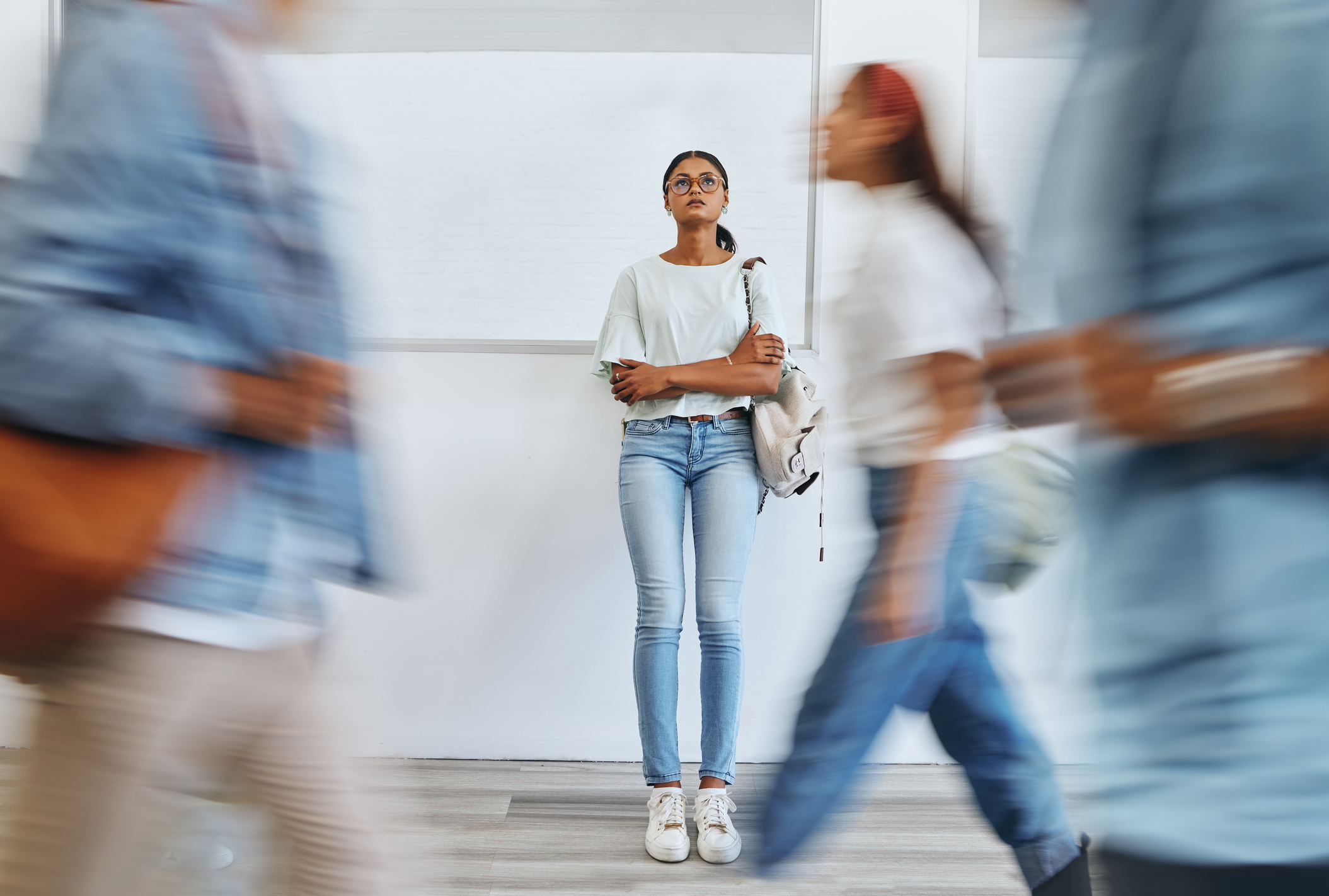 a woman stands alone in focus against a wall as blurry people speed past her