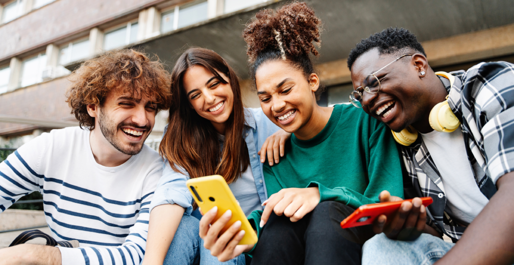 Group of friends laughing while looking at smartphones.