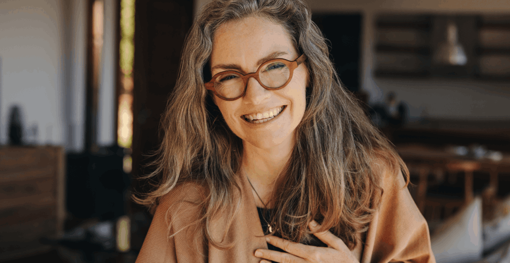 Smiling woman with glasses and long hair standing in a coffe shop.