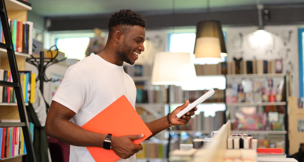 a man holds two books as he looks for more in a library