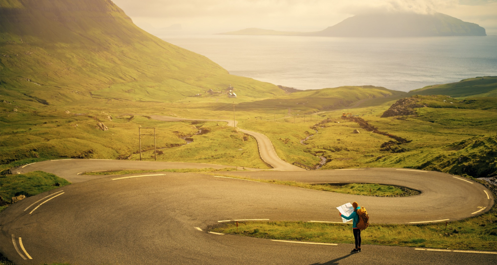 a person holding a map stands at the beginning of a long and winding path, seeming lost