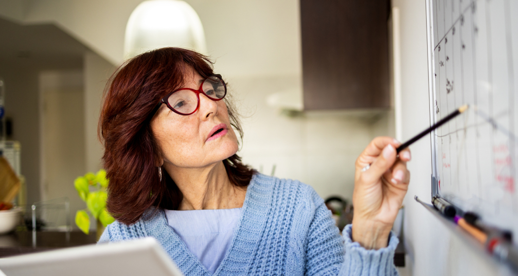 a woman holds her laptop in one hand and checks her wall calendar with the other