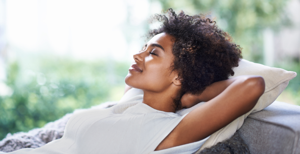 Woman relaxing on a couch with hands behind her head.